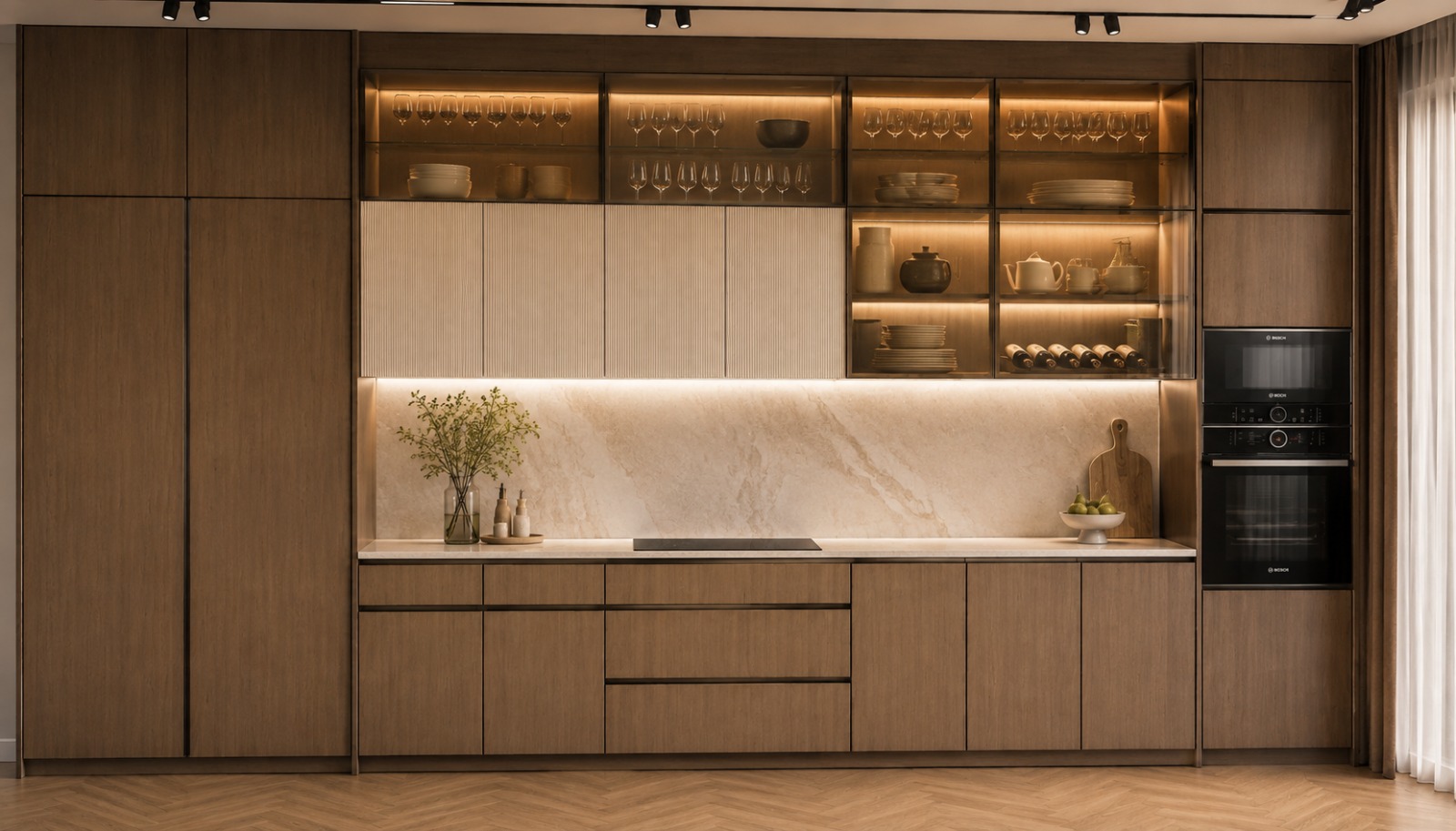 A kitchen wall in walnut with fluted cream doors, lit glass cabinets of glassware and china, a marble splashback and worktop, and built-in ovens